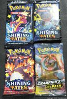 Front view of four sealed Pokémon Trading Card Game booster packs: three Shining Fates and one Champion's Path.