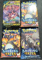Front view of four sealed Pokémon Trading Card Game booster packs including Sword & Shield Darkness Ablaze and Shining Fates editions.