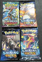 Four sealed Pokémon Trading Card Game booster packs including Sun & Moon Guardians Rising and Shining Fates editions with artwork of Decidueye, Charizard, and Eternatus.