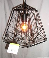 Close view of black iron geometric bird cage style lamp lit with Edison bulb, showing wire frame design and bulb detail.