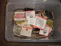 Top view of half-full clear plastic wheeled bin filled with assorted printed drink coasters, showing brands like Senior Service and Holsten.