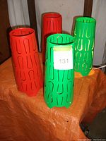 Four MCM style metal lamps, two green with fixtures and two orange shades only, standing on an orange surface.