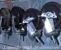 Four swivel caster wheels shown from side angle, two have brake levers and two do not, positioned side by side.
