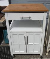 Front view of the white wooden microwave stand showing the wooden top, single drawer, open shelf, and double-door cabinet with repaired door.