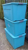 Three large teal plastic Sterilite storage bins stacked outdoors, showing size and shape.