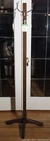 Full view of the vintage dark stained wood coat tree standing against white double doors on a wooden floor.