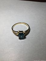 Front view of yellow gold ring with rectangular light blue stone on white background, showing the gemstone and band details.