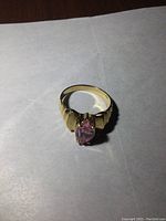 Front view of ring on white paper showing pink stone and scalloped shoulders