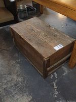 Side angle showing the rectangular wooden crate with visible aged wood grain and reinforced corner slats, positioned beside a wooden table.