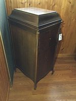 Full view of antique wooden gramophone showing side and front panels with missing knobs and crank handle on side.
