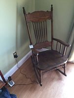 View of antique solid wood rocking chair showing pressed back design, spindle back slats, curved armrests, and contoured seat.