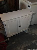 Front view of white two-door over the toilet bathroom cabinet on a concrete floor.