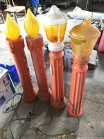Four vintage orange blow mold Christmas candle decorations with yellow flame and amber lantern tops. Visible cords for lighting. One candle shows damage on the top.