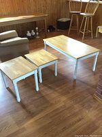Photo showing the full set of three tables arranged on wood floor with visible white legs and natural wood tops.