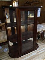 Front and side views of wood Bombay display cabinet with glass front door and open sides with semi-circular shelves, showing dark polished wood finish and tiered shelving.