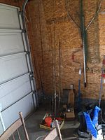 Four fishing rods with reels and one rod without reel standing against wall, tackle box and boots on floor