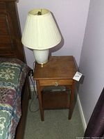 Wooden night table beside bed with white ceramic lamp on top, shows entire table and lamp setup.