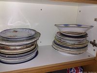 Two stacks of assorted plates in various designs and sizes arranged inside a cabinet.