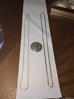 View of both sterling silver chains laid flat on white paper with sterling silver floral brooch in the center.