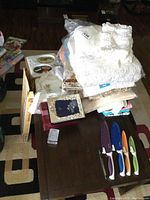 Overview of lot showing assorted linens, towels, placemats, frames, porcelain dish, and Starfrit cutters with sheaths