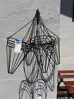 Photo showing the front view of the four hanging wrought iron planters with their chain hangers and shadow cast on white wall.