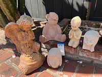 Wide shot of the five cement garden figurines including the tall praying angel and four smaller child and animal figurines on a brick patio.