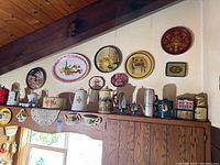 Wide view of kitchen wall above cabinets showing assortment of decorative trays, plates, canisters, and ceramic kitchen collectibles.
