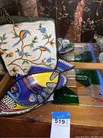 Porcelain fish-shaped dish with bright colors and intricate patterns alongside a porcelain floral bird tray and glass trays with green and blue geometric segments.
