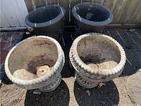 Overview of the four planters showing two ornamental pedestal planters and two larger plain round planters outside with visible weathering and dirt inside.