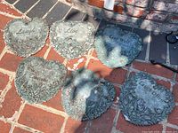 Six ceramic heart-shaped garden plaques with inscriptions including 'Laugh Often', 'Live Well', and 'Laugh'. Outdoors on brick surface. One plaque chipped on bottom.