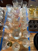 Photo showing assorted clear glassware including water or wine glasses, footed dessert bowls, and glass bowls on a wooden surface.