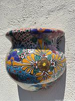 Front angle view showing colorful floral and geometric hand-painted design on ceramic wall planter with some shadows cast by sunlight.
