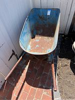 Front view of blue metal wheelbarrow showing rust inside basin and on handles.