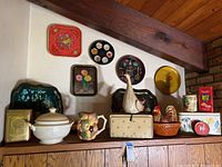 Overview of shelf containing vintage kitchen items including tureen, fruit pitcher, bread box with rooster, decorative trays, tins.