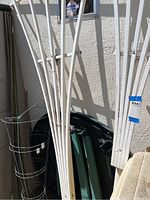 Photo showing white wooden trellises leaning against an exterior wall with part of a green foldable table and other garden elements visible, illustrating condition and contents of the lot.