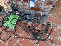 Five black metal planter hangers with varying degrees of rust and weathering placed on brick floor outside.