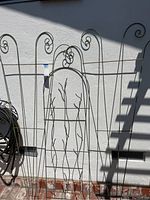Three metal garden trellises leaning against a wall, showing size, design, and condition with scroll tops and branch details.