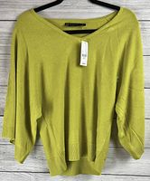 Front view of green women's sweater hanging on hanger against white wooden background, showing V-neck and loose fit.