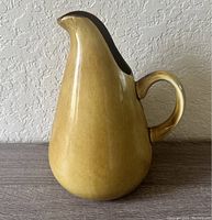 Side view of vintage ceramic pitcher with narrow spout and curved handle, olive green color