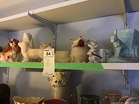 Shelf with several animal-themed ceramic planters including dog planters, mouse figurine, and a light blue goat pulling a cart planter.