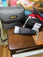 Bushnell binoculars in black carrying case, tripod in soft black bag on wooden table