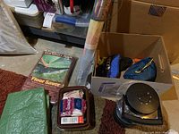 View of camping gear arranged on floor including Eureka Tent Floor Saver, folded green tarp, metal coffee cup, bags with first aid supplies, and other items