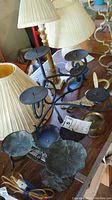 Photo showing four of the candle holders including the iron holder with 7 spiked plates and black metal holders among lamps.