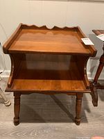 Front view of wooden end table showing scalloped edge on top, open lower shelf, turned legs, and side handles