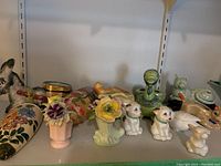Shelf showing assorted figurines including animal-shaped salt and pepper shakers, small flower figurines, lusterware flower vases.