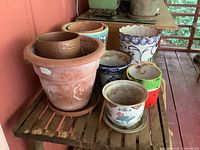 Overview showing eight flower pots on a wooden shelf including terracotta, ceramic, and watermelon-patterned pots