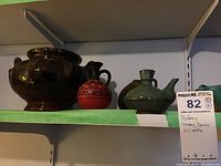 Shelving unit with large brown vase, small red decorative vase, green oil bottle, and other pottery items on the shelf