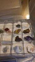 Clear acrylic box with twelve compartments displaying various mineral and quartz specimens placed on white padding.