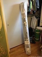 Rolled Pottery Barn rug wrapped in plastic leaning against a door in a closet area.