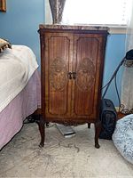 Full view of the 18th century wooden stand with marble top next to bed, showing carved legs, two-door front with floral inlay and metal handles, and the separate marble top.